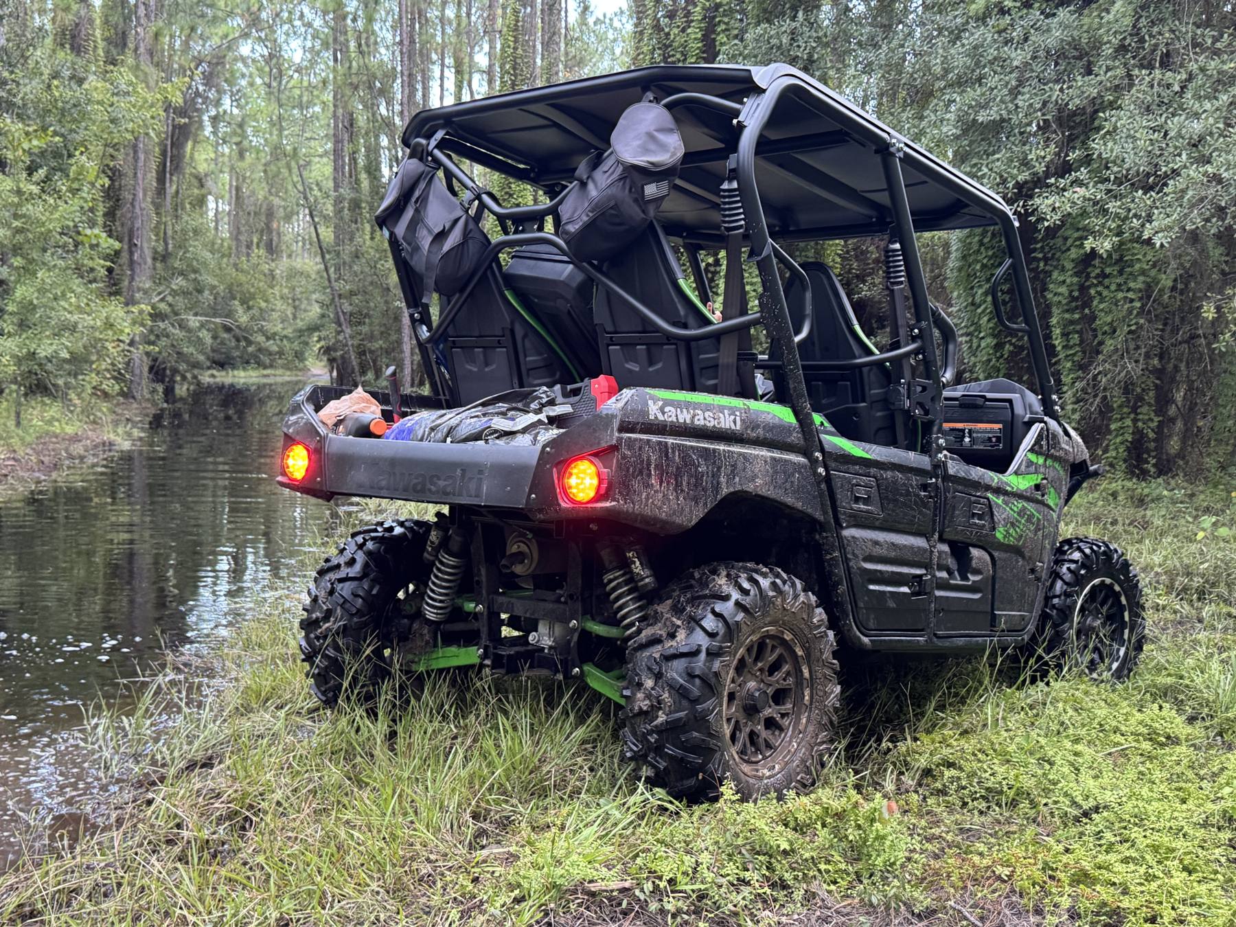 UTV Kawasaki verde parado na beira de um riacho em meio às árvores