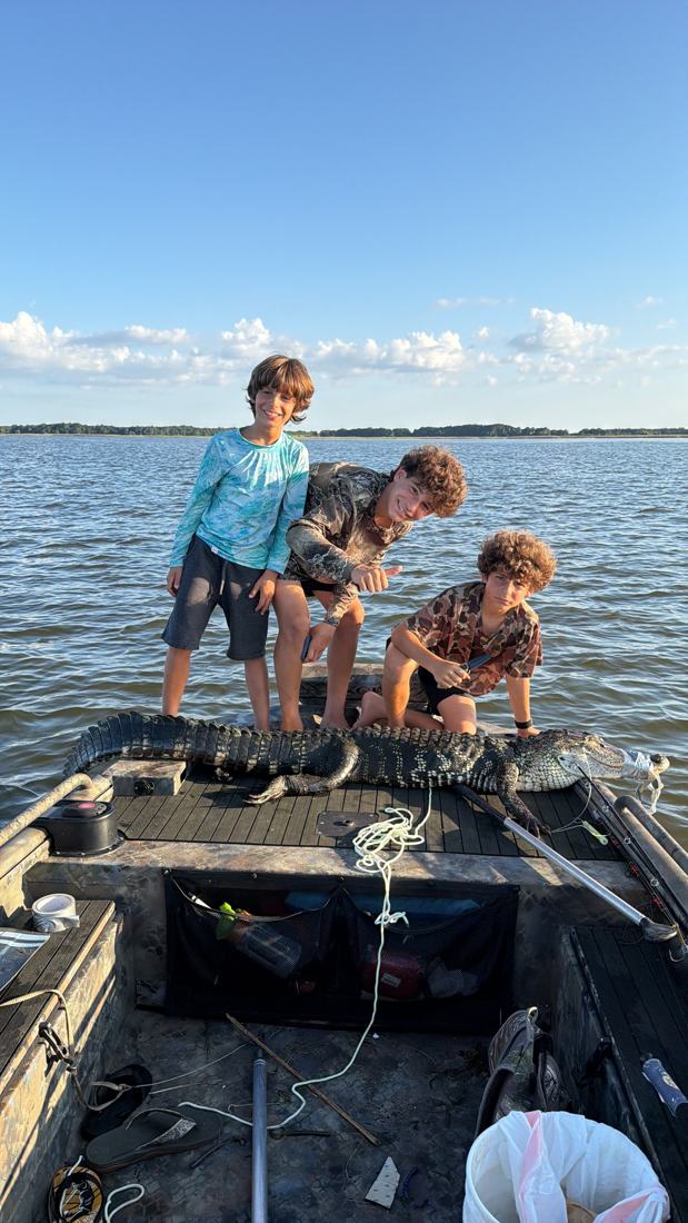 Três meninos de pé em um barco no meio de um lago, sob céu azul