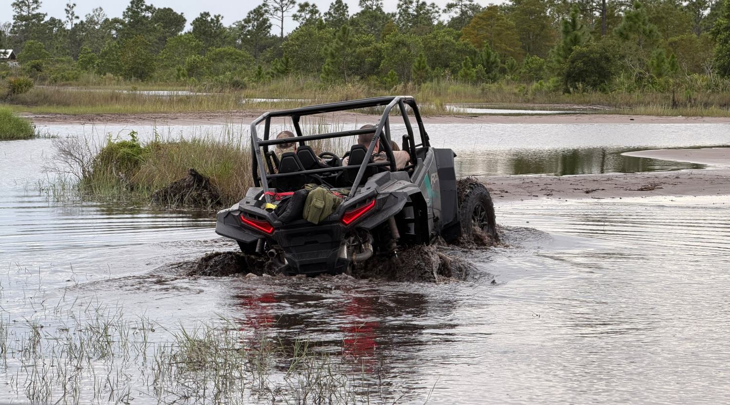 UTV Polaris atravessando uma área alagada, jogando lama e água, com pinheiros ao fundo