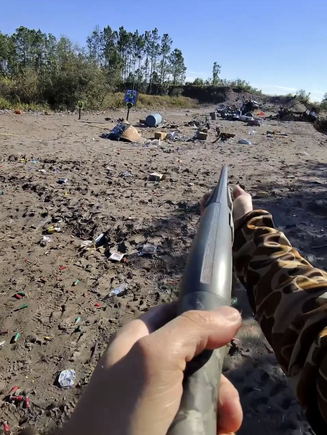 Cano de espingarda apontado para um range de areia com alvos e restos de cartuchos
