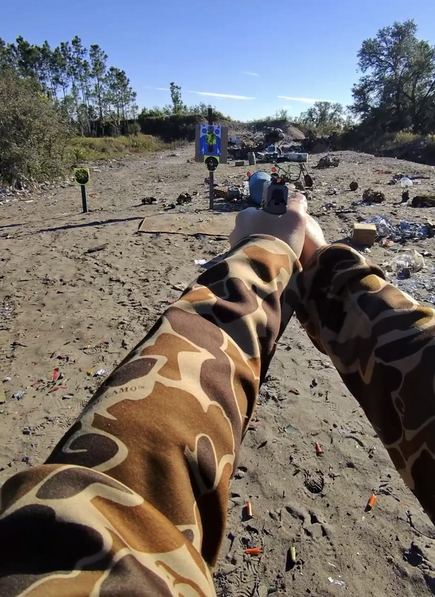 Braço de camuflagem apontando uma pistola para os alvos no range